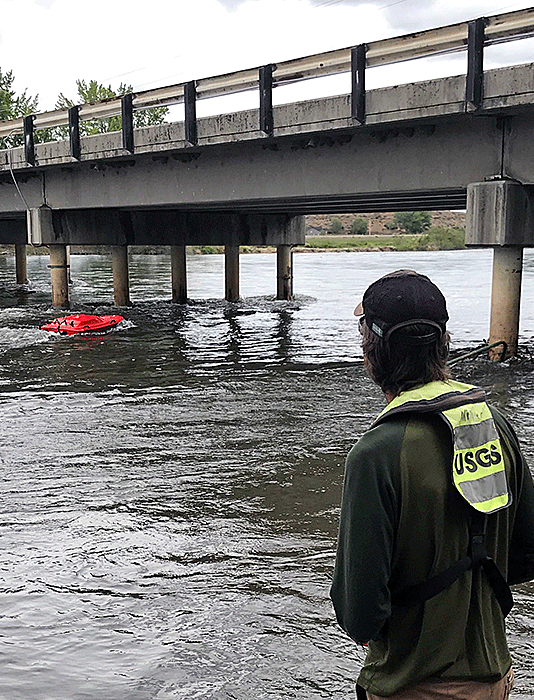 Hydrologic technician Russ Miller navigates a remote-controlled ADCP into position to measure streambed elevation at a highway bridge over the Payette River near Letha, Idaho.